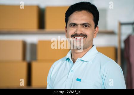 Heureux indien petit homme d'affaires confiant à la maison de vêtements de marchandises regardant la caméra - concept d'entrepreneur, démarrage réussi et gestionnaire. Banque D'Images