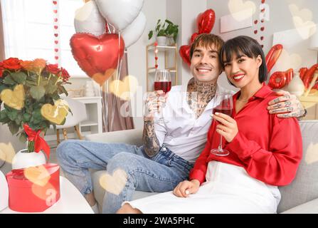 Jeune couple avec des verres de vin assis à la maison le jour de la Saint-Valentin Banque D'Images