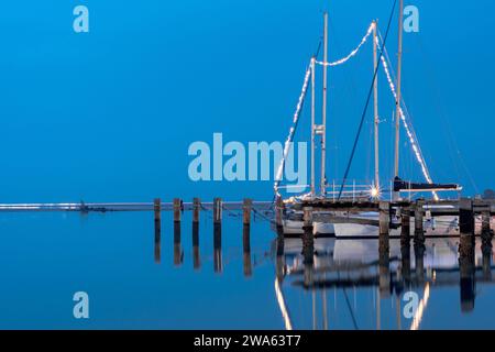 Photo de nuit avec longue exposition de Porto San Vito avec un voilier et des lumières de Noël sur tous les sommets. Grado mer en hiver avec un épais brouillard qui Banque D'Images