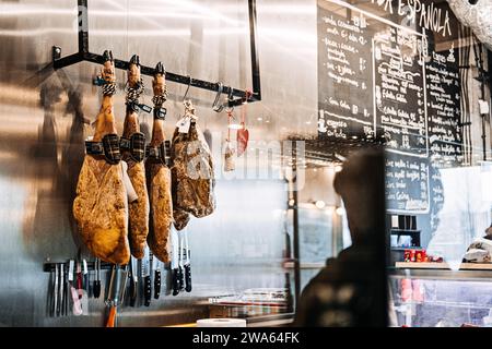 Jambons séchés suspendus dans une délicatessen espagnole. Des jambons traditionnels espagnols sont suspendus au-dessus d'un étalage de couteaux, dans une épicerie fine spécialisée. Varsovie Banque D'Images