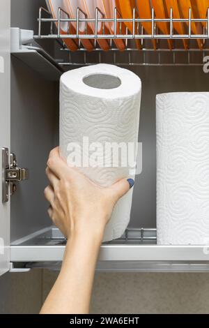 la main d'une femme sort une serviette en papier du placard. femme au foyer sort un rouleau d'essuie-tout de l'armoire de cuisine. Banque D'Images