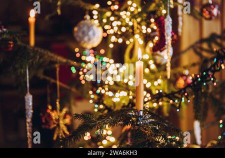 Focalisation sélective sur la combustion de bougie, clip de bougie sur le véritable arbre de Noël décoré avec des lumières de Noël bokeh sur fond. Banque D'Images