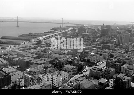 Blick über San Francisco mit der Oakland Bay Bridge, einigen Molen im Hafengebiet sowie dem Embarcadero Freeway, abgerissen 1991, vom Coit Aussichtsturm auf dem Telegraph Hill aus, 1962. Vue sur San Francisco avec le Oakland Bay Bridge, quelques jetées dans la zone portuaire et l'Embarcadero Freeway, démolie en 1991, depuis la tour d'observation de Coit sur Telegraph Hill, 1962. Banque D'Images