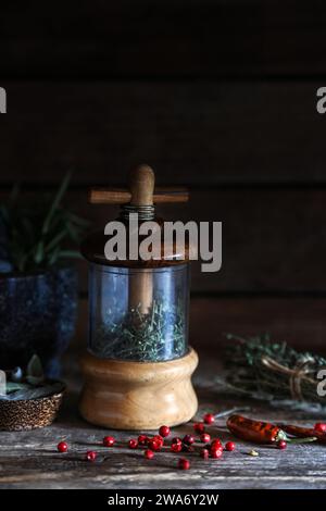 Moulin à herbes en bois vintage avec ingrédient à base de plantes mélangé de thym, sauge, piment rouge sur planche de bois - photographie sombre et moody Banque D'Images