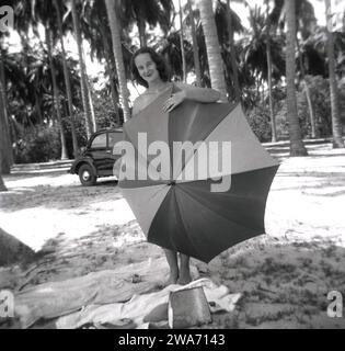 1953, historique, une jeune femme en vacances sur l'île de Ceylan, debout utilisant un parapluie pour cacher sa modestie sur la plage. Située dans l'océan Indien en Asie du Sud, l'île est devenue une République socialiste démocratique en 1972 et a changé son nom pour Sri Lanka. Banque D'Images