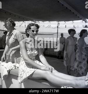 1953, historique, une jeune femme en vacances sur l'île de Ceylan (Sir Lanka) assise sur le côté sur un bateau avec ses jambes et les pieds sur la barrière. Banque D'Images