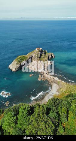 Vidéo aérienne par drone de Gaztelugatxeko San Joan baseliza, ermitage côtière à Biscaye en Espagne, avec un pont de pierre sinueux, un îlot rocheux et une vue sur le golfe de Gascogne Banque D'Images