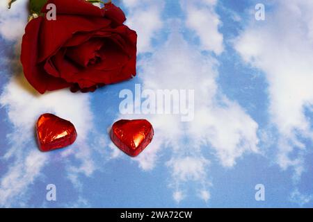 rose rouge et deux chocolats en forme de coeur sur un fond de motif de ciel Banque D'Images