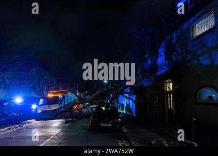 Beedell Avenue, Westcliff on Sea, Essex, Royaume-Uni. 2 janvier 2024. Les vents forts de la tempête Henk ont soufflé un arbre sur une voiture et une propriété, fermant la route. Les chirurgiens des arbres ont commencé à travailler pour enlever l'arbre, avec la police à portée de main créant la lumière bleue Banque D'Images