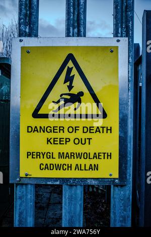 Panneau d'avertissement de danger de mort monté sur une clôture de sécurité de transformateur d'électricité. Le libellé est en anglais et en gallois. Banque D'Images