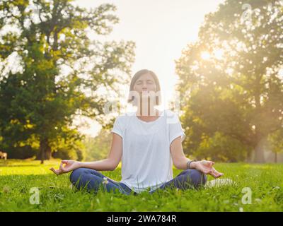 Jeune femme asiatique faisant de la méditation le matin ou le soir au parc, femme en bonne santé se détendant et pratiquant le yoga au parc de la ville. Pleine conscience, destinée, habitudes saines et concept d'équilibre Banque D'Images