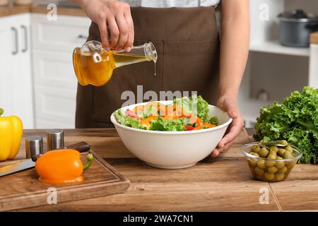 Femme ajoutant l'huile d'olive dans le bol avec salade savoureuse à la table dans la cuisine Banque D'Images