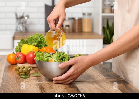 Femme ajoutant l'huile d'olive dans le bol avec salade savoureuse à la table dans la cuisine Banque D'Images