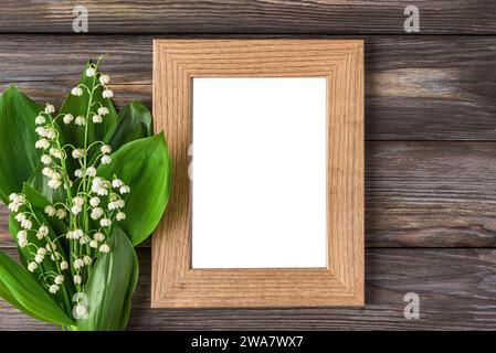 Cadre photo vierge avec bouquet de fleurs de printemps de lys de la vallée sur fond en bois rustique. Mariage, fête des femmes, carte de Saint Valentin. Maquette. Plat Banque D'Images