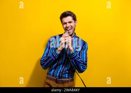 Portrait de gars positif habillé chemise élégante chantant la chanson lyrique dans le microphone au karaoké isolé sur fond de couleur jaune vif Banque D'Images