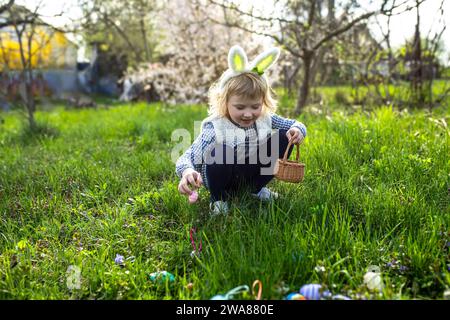 Fille porter des oreilles de lapin et recueillir des œufs de Pâques sur la chasse aux œufs de Pâques dans le jardin Banque D'Images