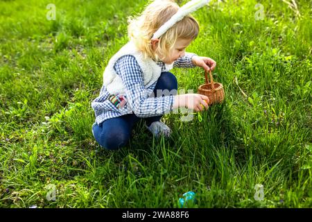 Petite fille qui recueille des œufs colorés dans le parc. Concept de chasse de Pâques Banque D'Images