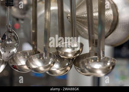 Ustensiles de cuisine en acier inoxydable suspendus dans une cuisine industrielle commerciale. Banque D'Images