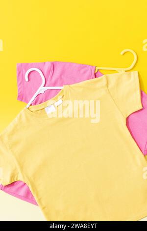 T-shirts pour enfants jaunes et roses sur fond jaune. Pose à plat. Banque D'Images