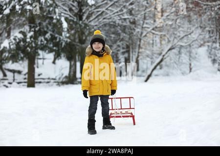 Petit garçon tirant luge à travers la neige dans le parc d'hiver Banque D'Images