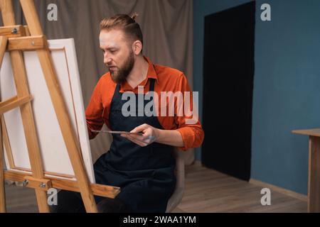 Bel homme peignant quelque chose de moderne sur sa toile blanche dans un studio d'art moderne Banque D'Images