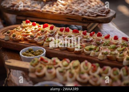 Petits sandwichs, canapés, servis lors d'un événement sur une planche de bois. Différents types visibles, végétariens et options de viande disponibles. Banque D'Images