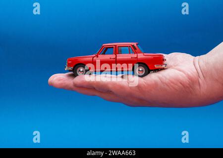 Main tenant la voiture de jouet rouge isolé sur fond bleu Banque D'Images