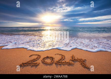 Lever de soleil de mer sur la plage de l'île tropicale et texte manuscrit dans le sable nouvel an 2024 Banque D'Images