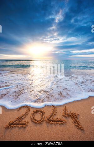 Lever de soleil de mer sur la plage de l'île tropicale et texte manuscrit dans le sable nouvel an 2024 vue verticale Banque D'Images