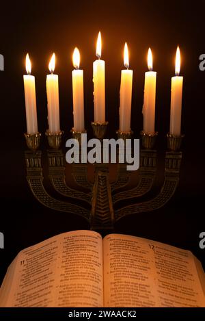 Sainte Bible ouverte au Livre d'Isaïe dans le Chapitre 11 et Menorah avec 7 bougies allumées isolées sur fond sombre. Banque D'Images