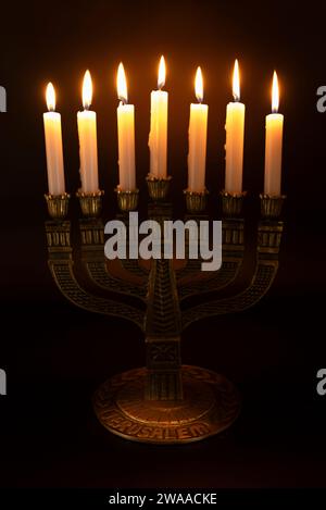 Menorah avec le mot JÉRUSALEM écrit sur sa base avec 7 bougies allumées isolées sur un fond sombre. Banque D'Images