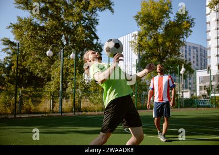 Joueur de football masculin frappant la balle avec son entraînement de poitrine sur le terrain de football de rue Banque D'Images