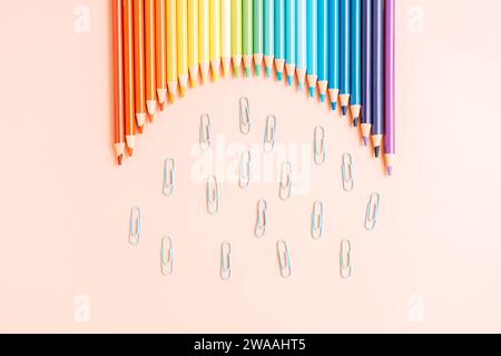 Crayons arc-en-ciel colorés se trouvent dans une rangée avec des trombones sur un fond beige Banque D'Images