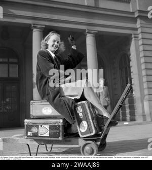 Dans les années 1940 Une jeune femme photographiée assise sur ses bagages, des valises les unes sur les autres sur un chariot de chemin de fer, attendant un taxi pour aller plus loin. 1948. Conard réf. 917 Banque D'Images