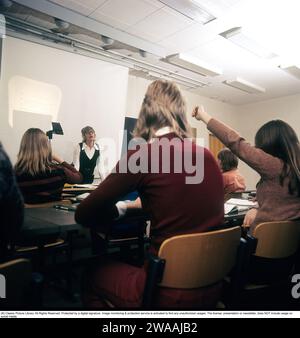 Dans les années 1970 Une classe scolaire est assise sur les bancs pendant une leçon avec une enseignante. Un rétroprojecteur se tient à l'avant, un dispositif commun dans les salles de classe à l'époque qui montrait la feuille transparente avec du texte et des images placées sur l'appareil sur l'écran. Les rétroprojecteurs étaient largement utilisés dans l'enseignement et les affaires avant l'avènement de la projection assistée par ordinateur. Suède années 1970 Banque D'Images