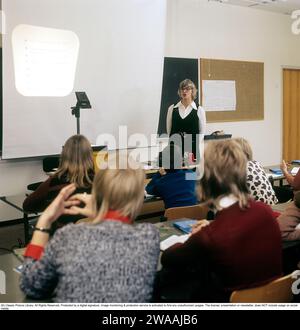 Dans les années 1970 Une classe scolaire est assise sur les bancs pendant une leçon avec une enseignante. Un rétroprojecteur se tient à l'avant, un dispositif commun dans les salles de classe à l'époque qui montrait la feuille transparente avec du texte et des images placées sur l'appareil sur l'écran. Les rétroprojecteurs étaient largement utilisés dans l'enseignement et les affaires avant l'avènement de la projection assistée par ordinateur. Suède années 1970 Banque D'Images