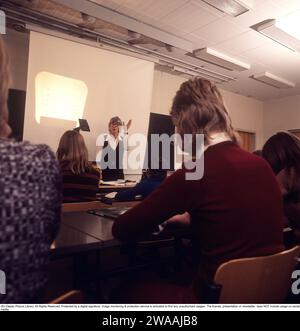 Dans les années 1970 Une classe scolaire est assise sur les bancs pendant une leçon avec une enseignante. Un rétroprojecteur se tient à l'avant, un dispositif commun dans les salles de classe à l'époque qui montrait la feuille transparente avec du texte et des images placées sur l'appareil sur l'écran. Les rétroprojecteurs étaient largement utilisés dans l'enseignement et les affaires avant l'avènement de la projection assistée par ordinateur. Suède années 1970 Banque D'Images