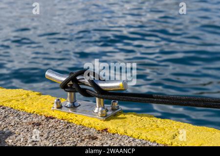 Corde d'amarrage noire avec une extrémité nouée attachée autour d'un taquet dans la marina de yacht. Attelage à crampons. Quincaillerie marine. Concept de yachting. Banque D'Images