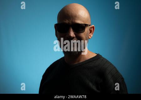 Portrait d'un homme mûr chauve et barbu portant des lunettes de soleil regardant vers l'appareil photo. Isolé sur fond bleu. Banque D'Images