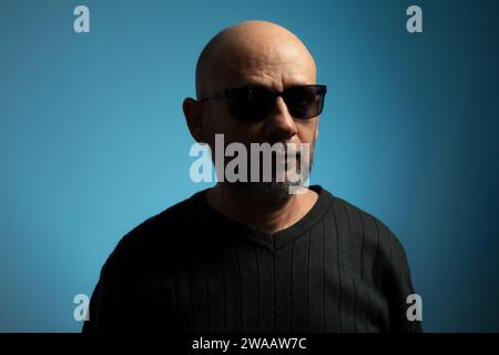 Portrait d'un homme mûr chauve et barbu portant des lunettes de soleil regardant vers l'appareil photo. Isolé sur fond bleu. Banque D'Images