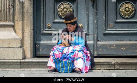 Cusco, Pérou - 24 octobre 2023 : femme péruvienne en vêtements traditionnels tricotant devant une porte près de la rue Banque D'Images