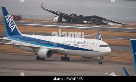 Tokyo, Japon. 03 janvier 2024. Un avion d'ANA taxi alors que les responsables enquêtent sur un Airbus A350 brûlé par Japan Airlines (JAL) après une collision avec un avion de la Garde côtière japonaise MA722 Mizunagi (Bombardier DHC-8-300) à l'aéroport international de Tokyo (aéroport Haneda) à Tokyo, Japon, le mercredi 3 janvier 2024. Photo de Keizo Mori/UPI crédit : UPI/Alamy Live News Banque D'Images