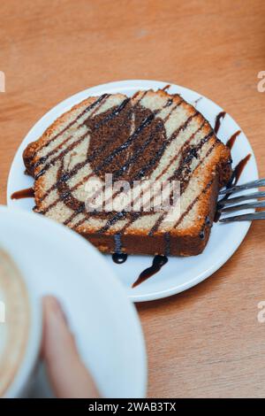 image verticale méconnaissable femme avec portion de pudding marbré sur plaque de porcelaine, avec tasse de café sur la table, pâtisserie et concept de café fo Banque D'Images