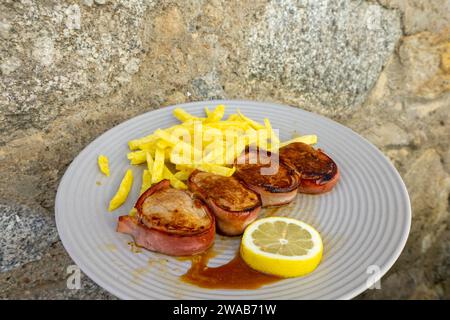 Délicieux filet de porc portugais enveloppé dans du bacon, servi avec des frites croustillantes. Banque D'Images