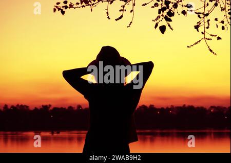 Silhouette d'une femme se détendant sur le lac contre ciel de couleur vive époustouflant Banque D'Images