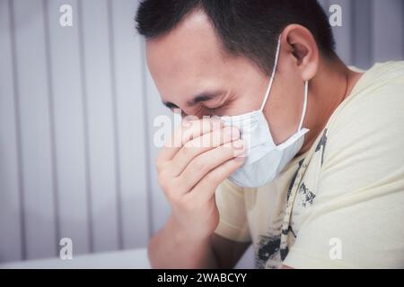 Un homme qui éternue dans un masque protecteur contre les maladies infectieuses transmissibles et comme protection contre la grippe en public. Coronavirus/covid- pandémique Banque D'Images