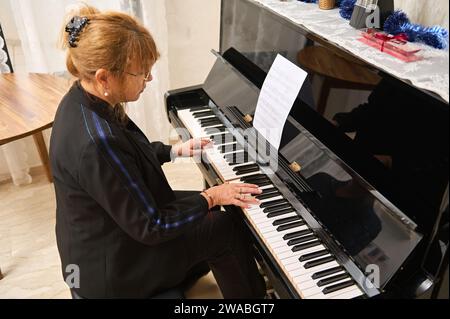 Vue aérienne d'une authentique femme asiatique mature en tenue décontractée noire, jouant du piano et chantant, enseignant leçon de piano à la maison. Les gens, les hobbies et Banque D'Images