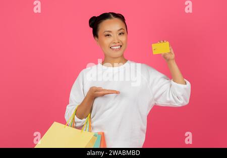 Concept de cashback. Heureuse femme asiatique posant avec carte de crédit et sacs à provisions Banque D'Images
