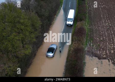 Offenham, Evesham, 3 janvier 2024 - Un conducteur de BMW a essayé et échoué de conduire dans les eaux de crue malgré un autre véhicule déjà abandonné sur le même tronçon. Le conducteur âgé a accéléré son moteur pendant qu'il conduisait, mais sa vitesse était trop grande et de l'eau est entrée dans son moteur. Le véhicule a finalement repris, mais il s'est heurté à un autre arrêt à quelques mètres de la terre ferme. Un travailleur de la voirie est alors arrivé et a placé un panneau « route fermée » devant son véhicule en guise d'insulte finale. C'est arrivé à côté d'Offenham caravaning Park qui est près d'Evesham dans le Worcestershire où la rivière Avon a des burs Banque D'Images