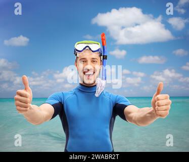 Guy en combinaison avec un masque de plongée faisant un geste pouce vers le haut près de la mer Banque D'Images